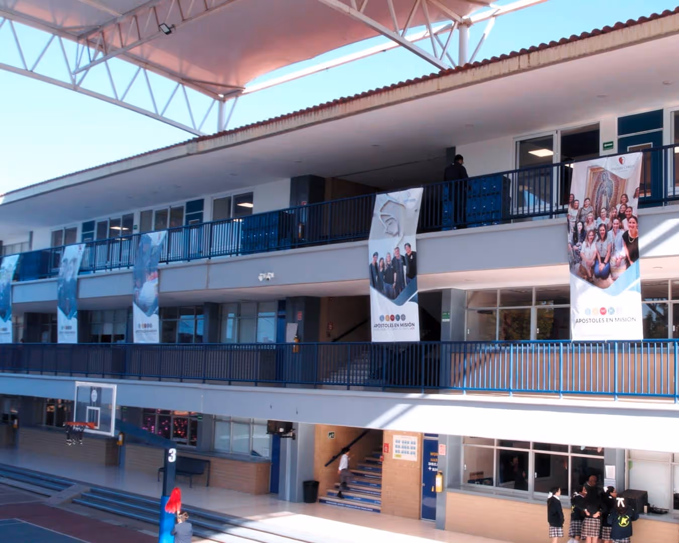 Una sala de conferencias moderna y bien iluminada, con filas de sillas acolchadas de color beige, una pantalla de proyección en la parte delantera y paredes verdes con un logotipo geométrico blanco. El techo tiene secciones azules y verdes.